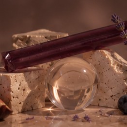 Rest jelly stick balanced on travertine beside a glass sphere and black grapes